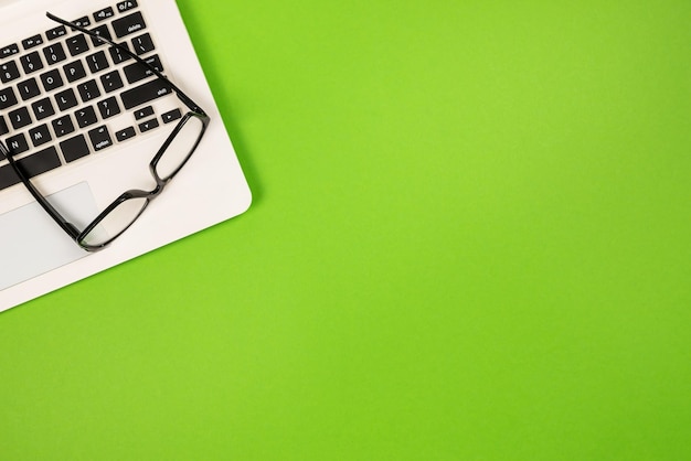 Vista dall'alto del laptop bianco con occhiali su sfondo verde isolato con spazio per la copia