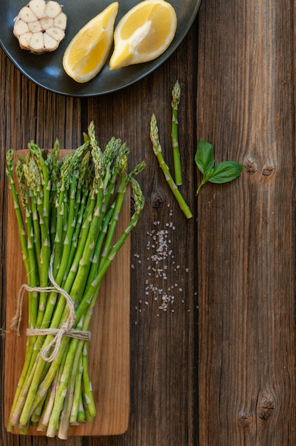 Vista dall&#39;alto del mazzo di asparagi verdi freschi con limone e aglio sul tavolo di legno