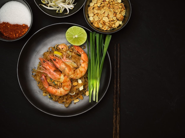 Vista dall'alto del Pad Thai, spaghetti tailandesi saltati in padella con gamberetti su piatto in ceramica nera con lime ed erba cipollina