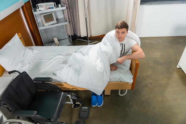 Vista dall'alto del paziente malato appoggiato al letto dell'ospedale coperto con trapunta in corsia ospedaliera. Concetto di assistenza sanitaria