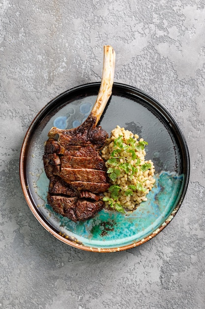 Vista dall'alto del piatto con bistecca di tomahawk alla griglia servita con orzo perlato