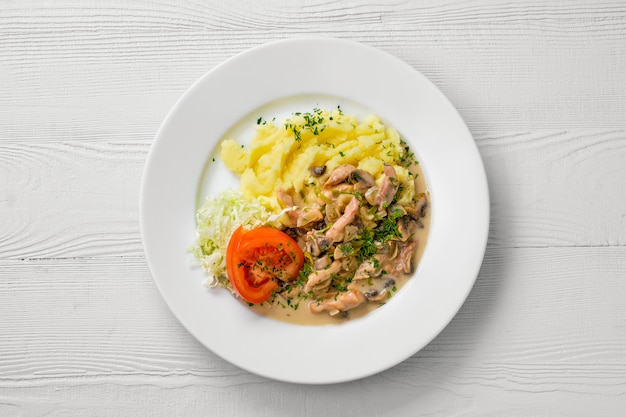 Vista dall'alto del piatto con gulasch di pollo, funghi, purè di patate e insalata di cavolo pomodoro