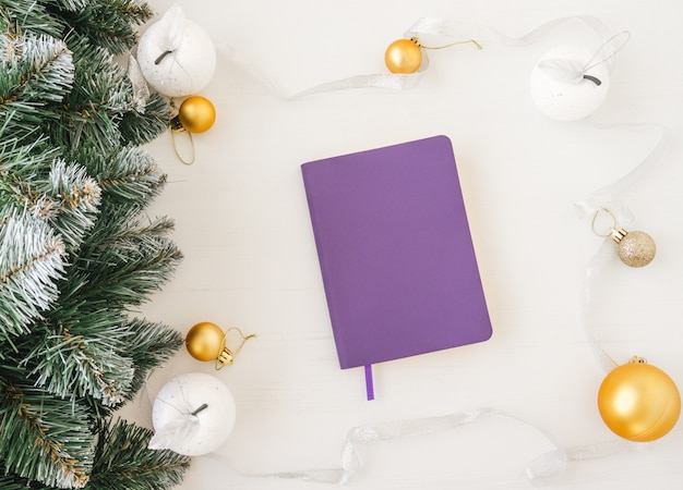 Vista dall'alto del quaderno viola all'interno del telaio fatto di decorazioni natalizie su fondo di legno bianco.