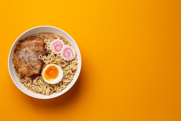 Vista dall'alto del ramen di zuppa di noodle giapponese in una ciotola bianca con noodles, brodo di carne, maiale arrosto a fette, narutomaki, uovo con tuorlo su sfondo arancione brillante. Piatto tradizionale del Giappone, spazio per il testo