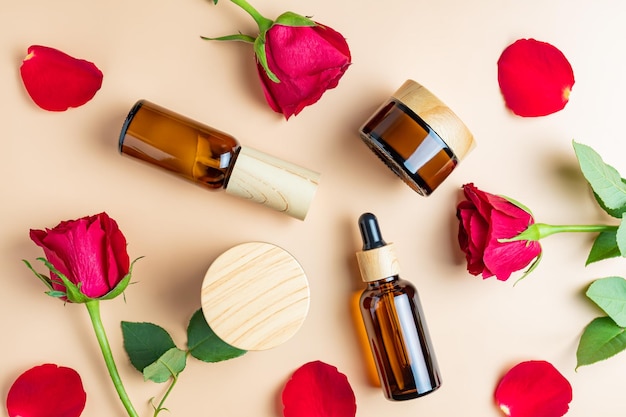 Vista dall'alto del set di cosmetici per la cura della pelle femminile Bottiglie e vasetti di vetro scuro con siero e olio per maschera crema Rose rosse in fiore come decorazione Concetto festivo per la donna presente