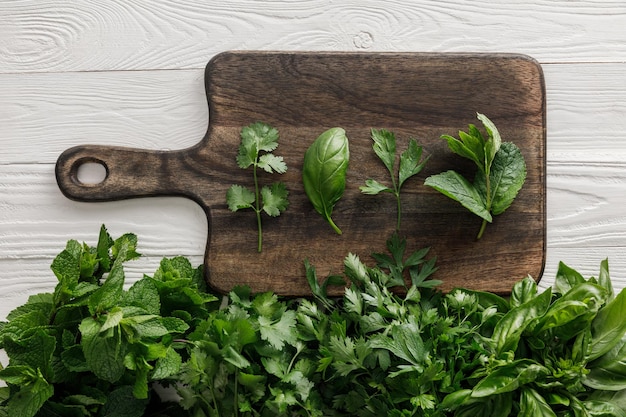 Vista dall'alto del tagliere di legno marrone con basilico prezzemolo coriandolo e foglie di menta piperita vicino