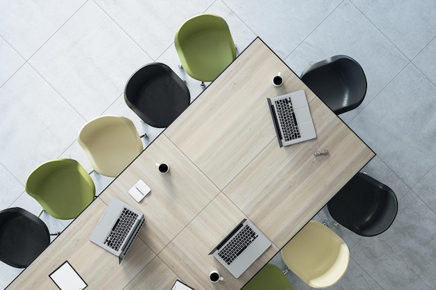 Vista dall'alto del tavolo da ufficio in legno disegnato con laptop, tazze da caffè, forniture e sedie