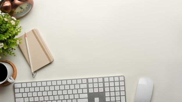 Vista dall'alto del tavolo del computer con tastiera, mouse, libro caseario, tazza di caffè, decorazioni e spazio di copia