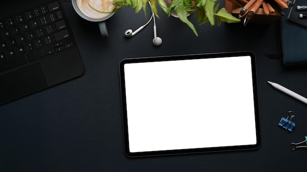 Vista dall'alto del tavolo digitale mockup con schermo vuoto, auricolare, tastiera e pianta su sfondo nero.