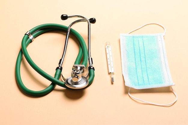 Vista dall'alto del termometro a mercurio dello stetoscopio e di una maschera protettiva su sfondo colorato Attrezzature mediche e concetto di assistenza sanitaria