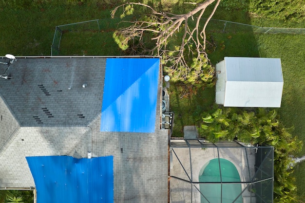 Vista dall'alto del tetto di una casa che perde coperto con teloni protettivi contro le perdite di acqua piovana fino alla sostituzione delle tegole di asfalto Danni al tetto dell'edificio a seguito dell'uragano Ian in Florida