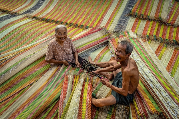 Vista dall'alto del vecchio artigiano amante vietnamita che realizza con felicità le tradizionali stuoie del vietnam