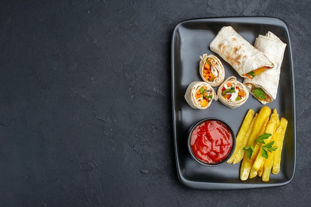 Vista dall'alto delizioso panino pita affettato shawarma con patatine fritte e ketchup su superficie scura