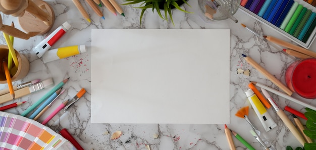 Vista dall'alto dell'area di lavoro dell'artista moderno con carta da schizzo e strumenti di pittura sulla scrivania in marmo