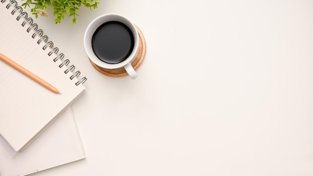 Vista dall'alto dell'area di lavoro moderna con una tazza di caffè a matita blocco note e copia spazio su sfondo bianco