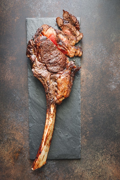 Vista dall'alto della bistecca di manzo in marmo essiccato Tomahawk su ardesia nera con spezie Concetto di cena piatta