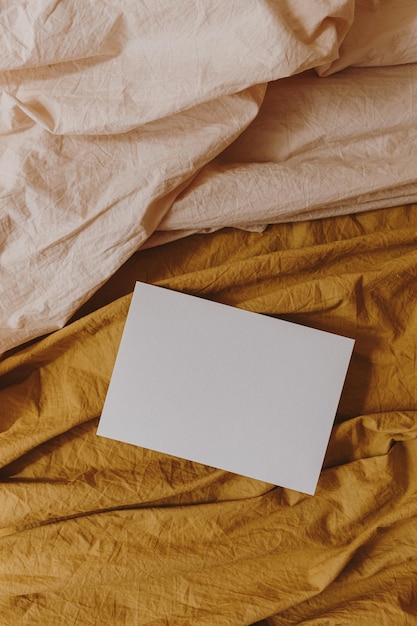 Vista dall'alto della carta del foglio di carta bianca con lo spazio della copia mockup sul panno di coperta di lino beige e zenzero Flatlay estetico Modello di carta di invito matrimonio elegante minimalista