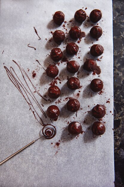 Vista dall'alto della composizione con tartufi di cioccolato e strumento di cioccolato cosparso di cacao in polvere su carta da forno bianca pergamena