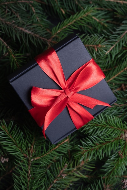 Vista dall'alto della confezione regalo di Natale nera con nastro rosso su sfondo abete. Tempo per il concetto di vacanza. Foto di alta qualità