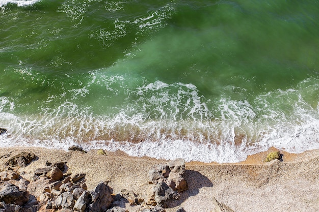 Vista dall'alto della costa del mare con acqua verde e surf su una spiaggia sabbiosa.