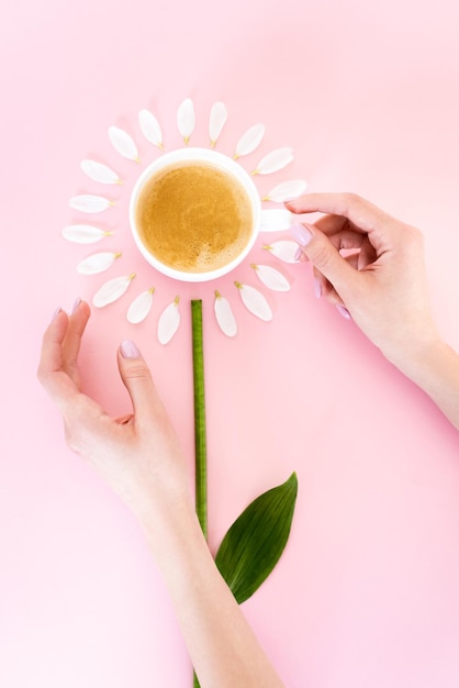 Vista dall'alto della donna che tocca la tazza di caffè vicino ai petali di fiori bianchi sul concetto di festa della mamma rosa