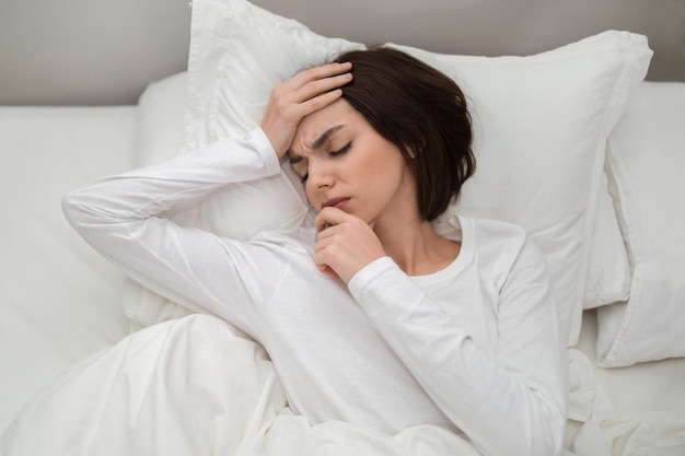 Vista dall'alto della donna infelice sdraiata a letto che tocca la testa