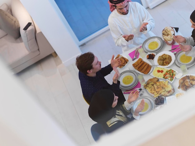 Vista dall'alto della famiglia musulmana che fa iftar dua per rompere il digiuno durante il Ramadan. Popolo arabo che tiene le mani in gesto per pregare e ringraziare Allah prima della cena tradizionale