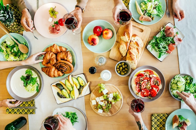 Vista dall'alto della festa della gente a tavola ricoperta di cibi e bevande con piatti, insalate, frutta, verdura, vino e salse