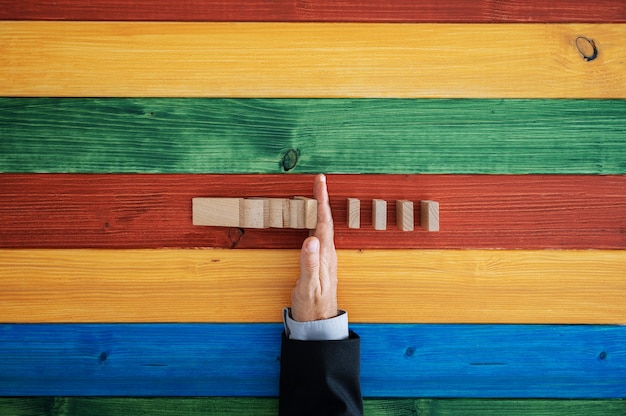 Vista dall'alto della mano maschile che ferma l'effetto domino su sfondo di legno colorato.