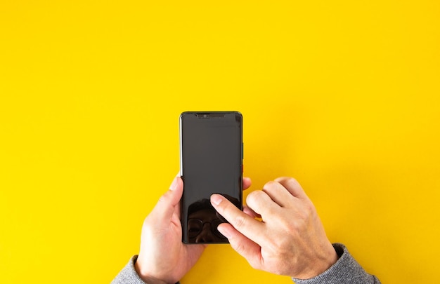 Vista dall'alto della mano maschile che tiene lo smartphone con sfondo di colore giallo con spazio per la copia