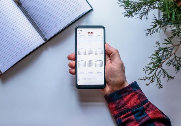 Vista dall'alto della mano maschile con il cellulare con un calendario per il 2023