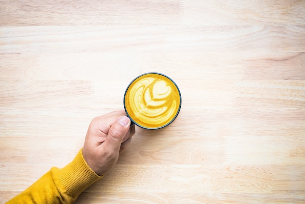 Vista dall'alto della mano maschio che tiene tazza di caffè su legno