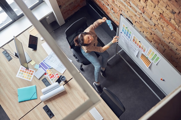 vista dall'alto della moderna designer femminile che seleziona i colori dai campioni guardando il progetto