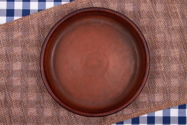 Vista dall'alto della padella di argilla rotonda vuota sul tavolo coperto con tovaglia a scacchi e tovagliolo di saccheggio