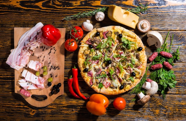 Vista dall'alto della pizza su un tavolo di legno circondato da verdure, funghi e formaggio vicino al tagliere con carne