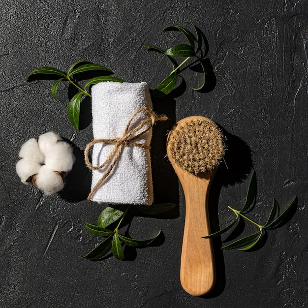 Vista dall'alto della spazzola massaggiante in legno con setole naturali e asciugamano arrotolato bianco pronto per le procedure termali domestiche. Accessori personali