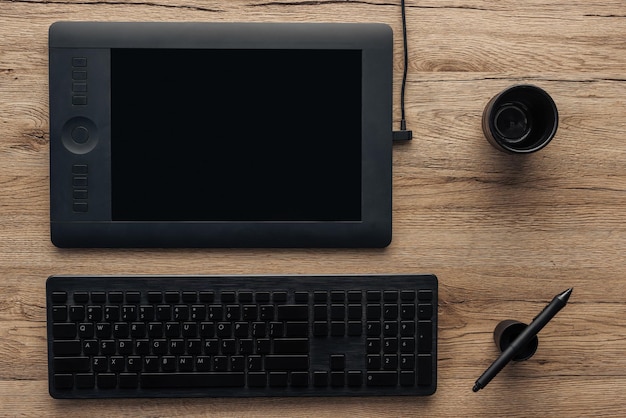 Vista dall'alto della tastiera del computer wireless con penna grafica nera e tazza vuota su legno