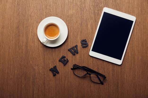 Vista dall'alto della tavoletta digitale con schermo vuoto vicino a notizie scritte tazza di caffè e bicchieri