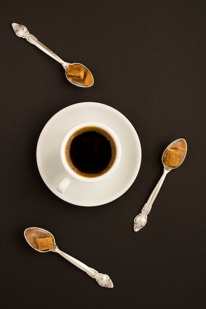 Vista dall'alto della tazza di caffè e dei cucchiai con lo zucchero sulla tavola nera. Avvicinamento.