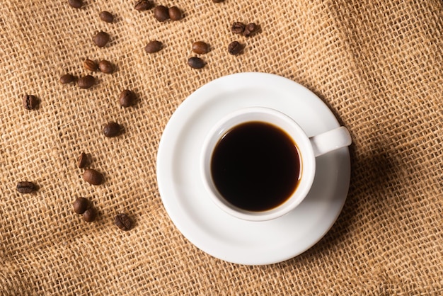 Vista dall'alto della tazza di caffè sulla tovaglia di iuta decorata con chicchi di caffè