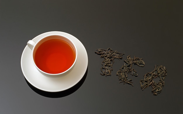 Vista dall'alto della tazza di tè in ceramica bianca e foglie di tè essiccate su sfondo scuro con spazio per la copia per il testo.