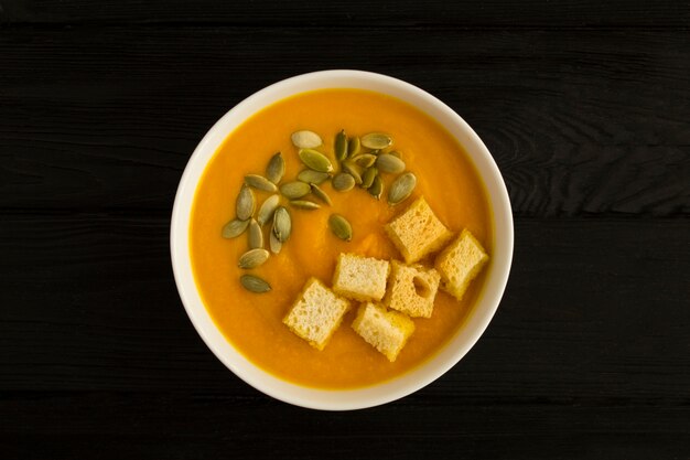 Vista dall'alto della zuppa di zucca con semi e cracker nella ciotola bianca