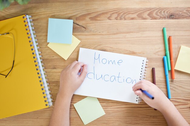 Vista dall'alto delle mani del ragazzo della scuola dell'America latina che scrive Educazione domestica sulla carta usando le matite durante lo studio a casa. Concetto di homeschooling