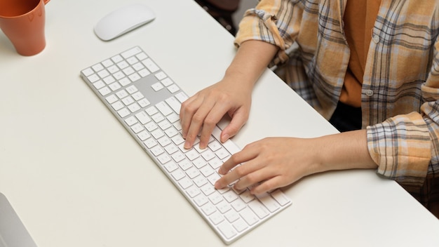 Vista dall'alto delle mani delle donne freelance che digitano sulla tastiera del computer sul tavolo bianco nella stanza dell'ufficio domestico