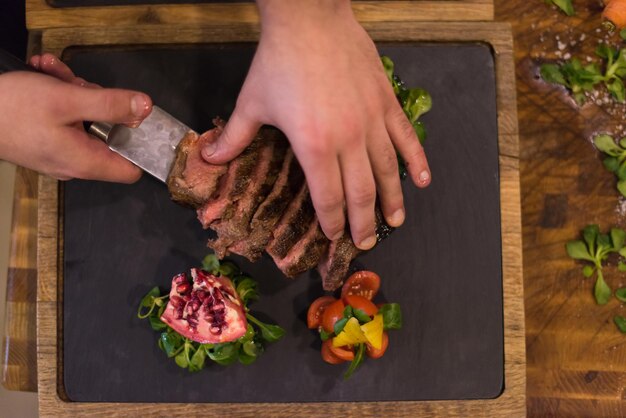 vista dall'alto delle mani dello chef nella cucina dell'hotel o del ristorante che preparano bistecca di manzo con decorazione vegetale