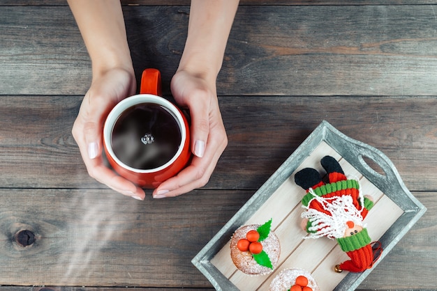 Vista dall'alto delle mani di una donna che tiene calda tazza di caffè sul tavolo in legno con decorazioni natalizie