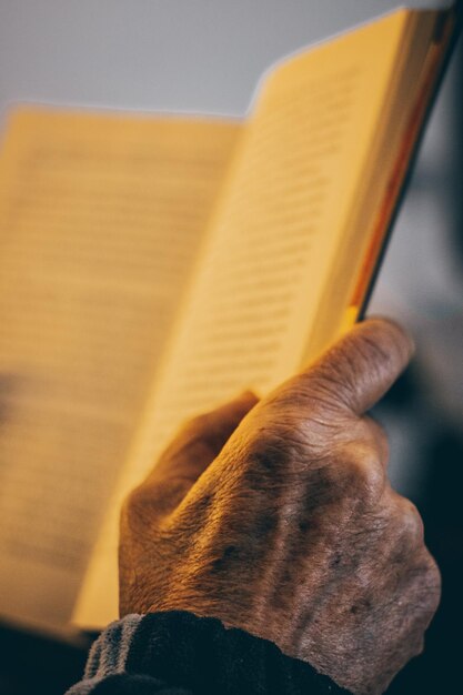 Vista dall'alto delle mani di una persona anonima che tiene un libro aperto e legge durante il giornoxA