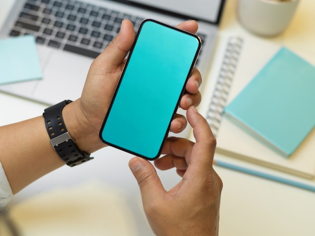 Vista dall'alto delle mani di uomo d'affari che tengono smartphone mentre era seduto al lavoro