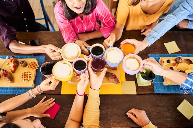 Vista dall'alto delle mani ravvicinate di persone multiculturali che fanno colazione bevendo caffè e applausi felici