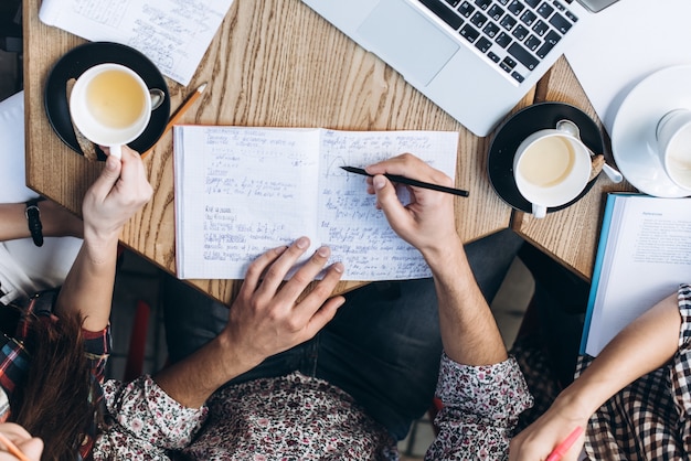 Vista dall&#39;alto delle persone che studiano con il libro di libro, il libro e il computer portatile. Tazze di caffè sul tavolo